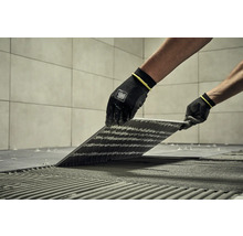 Obkladač kladie dlaždice pomocou špeciálneho náradia a ochranného odevu.