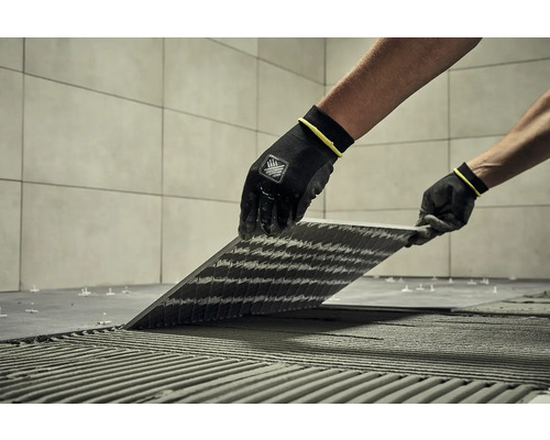 Obkladač kladie dlaždice pomocou špeciálneho náradia a ochranného odevu.