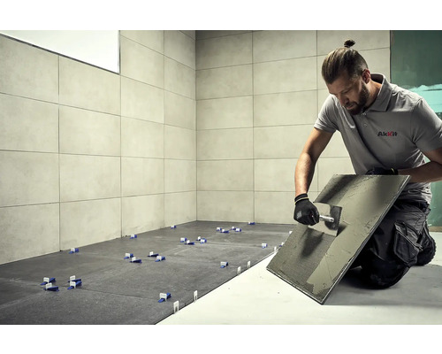 Obkladač pri práci, dlaždice, náradie a logo AkKit