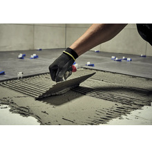 Obkladač s hladidlom nanáša lepidlo na dlaždici, aby ju položil