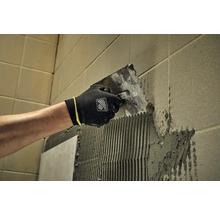 Obkladač nanáša lepidlo na stenu pomocou špachtle