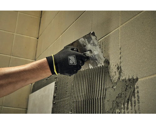 Obkladač nanáša lepidlo na stenu pomocou špachtle