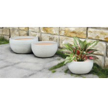 Tri okrúhle kvetináče vonku pred kamennou stenou.