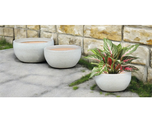 Tri okrúhle kvetináče vonku pred kamennou stenou.