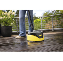 Osoba čistí drevenú terasu čističom povrchov.