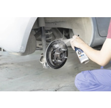 Osoba čistí otvorenú bubnovú brzdu automobilu čističom bŕzd.