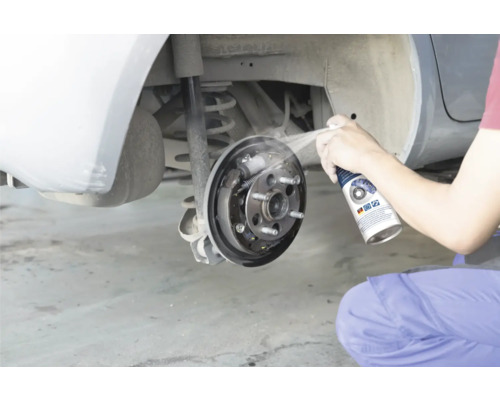 Osoba čistí otvorenú bubnovú brzdu automobilu čističom bŕzd.