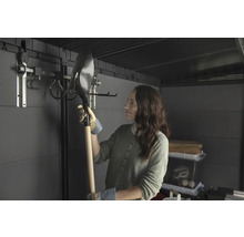 Žena drží lopatu v záhradnom domčeku so systémom na zavesenie náradia