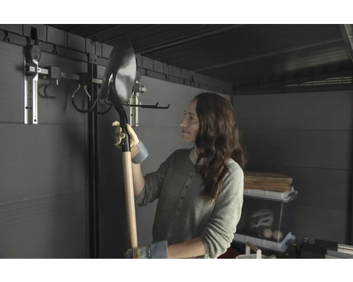 Žena drží lopatu v záhradnom domčeku so systémom na zavesenie náradia