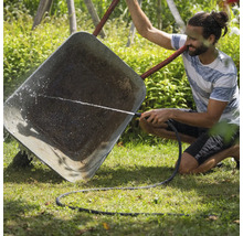 Muž čistí fúrik záhradnou hadicou.
