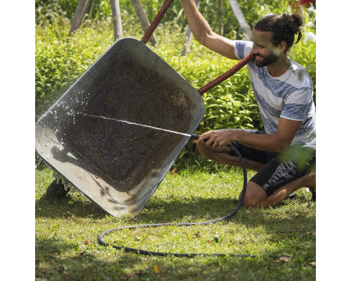Muž čistí fúrik záhradnou hadicou.