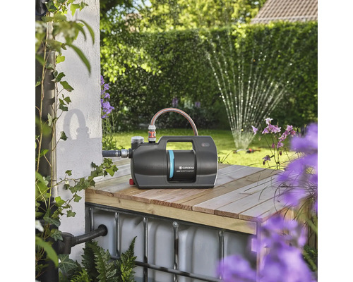 Záhradné čerpadlo Gardena na drevenej konštrukcii so záhradou v pozadí.