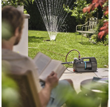 Záhrada so záhradným čerpadlom a zavlažovačom trávnika, zatiaľ čo si osoba číta knihu