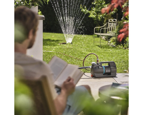 Záhrada so záhradným čerpadlom a zavlažovačom trávnika, zatiaľ čo si osoba číta knihu