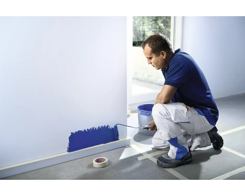 Muž valčekom maľuje stenu v miestnosti.