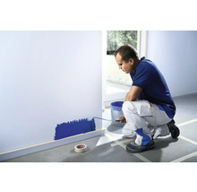 Muž maľuje valčekom stenu, okolo je maskovacia páska.