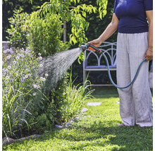 Osoba zalieva rastliny v záhrade záhradnou hadicou.