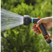 Ruka drží záhradný postrekovač, z ktorého strieka voda.