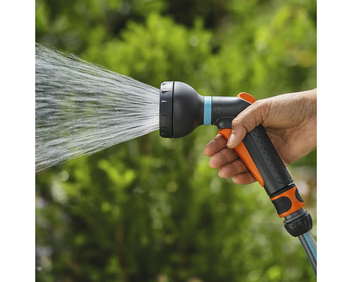 Ruka drží záhradný postrekovač, z ktorého strieka voda.