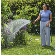 Žena zavlažuje záhradné rastliny záhradnou hadicou a striekacou pištoľou.