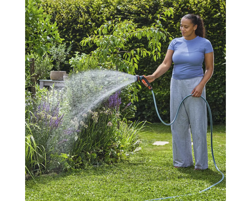 Žena zavlažuje záhradné rastliny záhradnou hadicou a striekacou pištoľou.