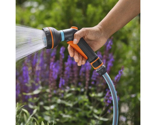 Ruka drží striekaciu pištoľ záhradnej hadice s vodným lúčom