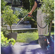 Osoba zalieva rastliny záhradnou striekacou pištoľou v záhrade.