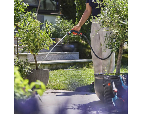 Osoba zalieva rastliny záhradnou striekacou pištoľou v záhrade.
