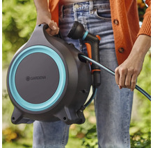 Osoba drží hadicový box Gardena so záhradnou hadicou a postrekovačom.