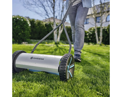 Ručná kosačka na trávu s osobou v záhrade.