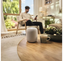 Inteligentný reproduktor na okrúhlom drevenom stole v obývacej izbe