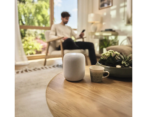 Inteligentný reproduktor na okrúhlom drevenom stole v obývacej izbe