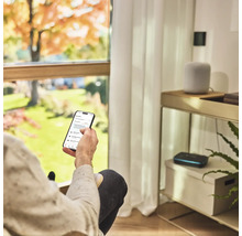 Osoba s inteligentným telefónom na ovládanie zavlažovania záhrady v obývacej izbe.