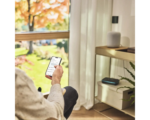 Osoba s inteligentným telefónom na ovládanie zavlažovania záhrady v obývacej izbe.