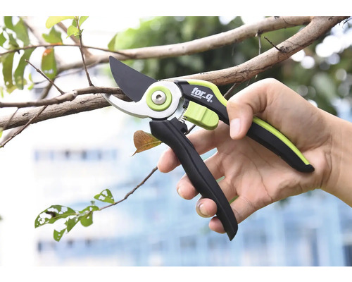 Osoba drží záhradnícke nožnice značky for_q pri prerezávaní konára.