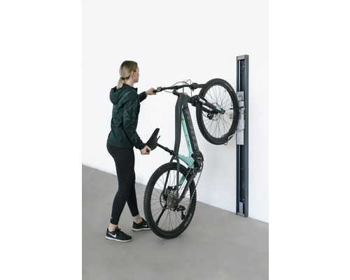 Žena zavesuje elektrický horský bicykel na nástenný držiak.