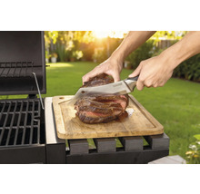 Pripravený steak sa krája nožom na drevenej doske vedľa grilu.