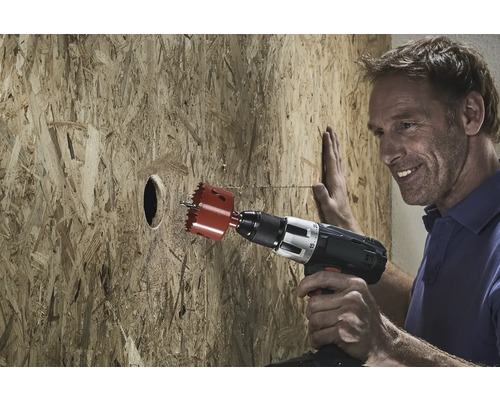 Muž vŕta otvor do drevenej dosky pomocou dierovky