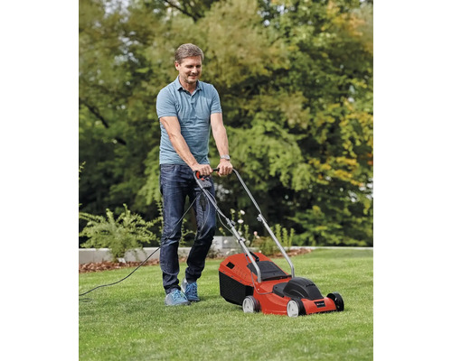 Muž kosí trávnik elektrickou kosačkou.