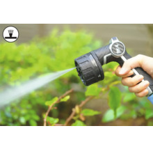 Ruka drží striekaciu pištoľ záhradnej hadice pri zalievaní rastlín