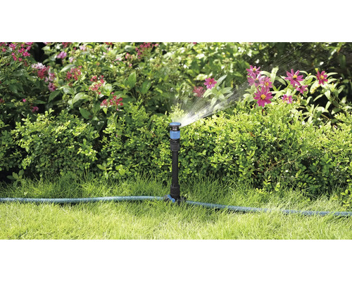 Záhradná scéna so zavlažovačom trávnika, ktorý zavlažuje rastliny