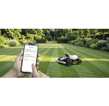 Scéna s robotickou kosačkou na trávniku a osobou používajúcou smartfón na ovládanie zariadenia