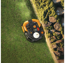 Pohľad zhora na robotickú kosačku na trávniku vedľa kamennej steny