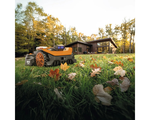 Robotická kosačka na trávniku s lístím pred obytným domom.