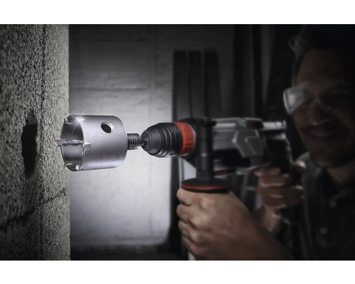 Muž vŕta dieru do betónovej steny pomocou dierovacej píly.