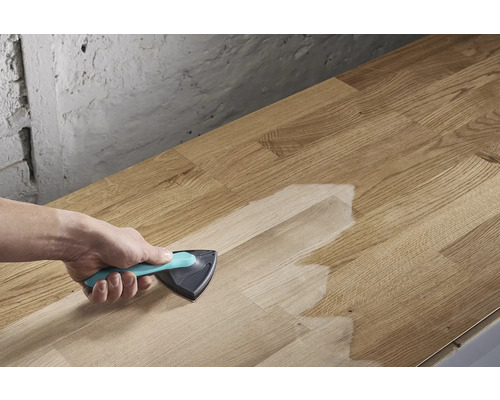 Osoba nanáša povrchovú úpravu trojuholníkovou kefou na drevenú dosku.