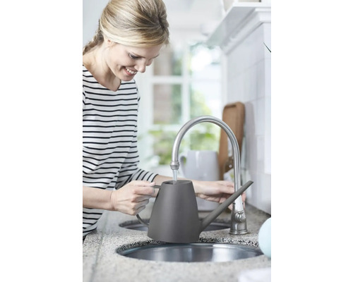 Žena plní sivú kanvicu na polievanie pri vodovodnom kohútiku