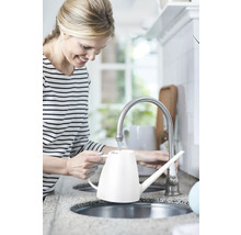 Žena plní bielu kanvicu na zalievanie pri vodovodnom kohútiku v kuchyni.