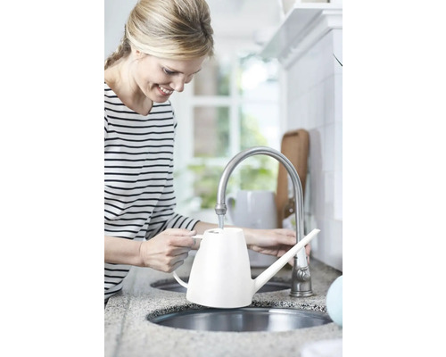 Žena plní bielu kanvicu na zalievanie pri vodovodnom kohútiku v kuchyni.