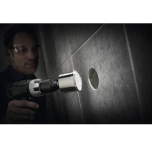 Muž vŕta dierovačkou s diamantovou korunkou otvor do dlaždice.